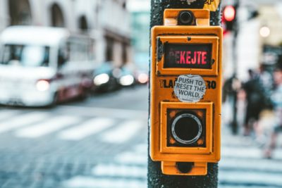 street crosswalk button with sticker saying "press to reset the world"
